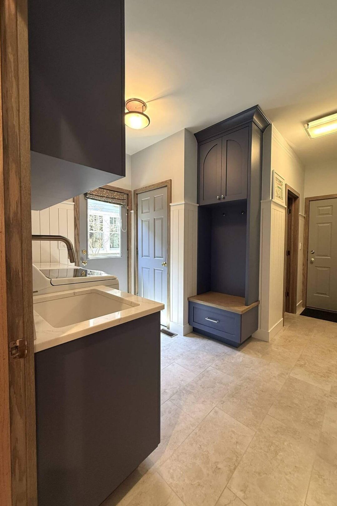 Mudroom room with navy blue built-in bench, upper locker cabinet, laundry sink, and dark cabinetry - Kelly Thayer Design