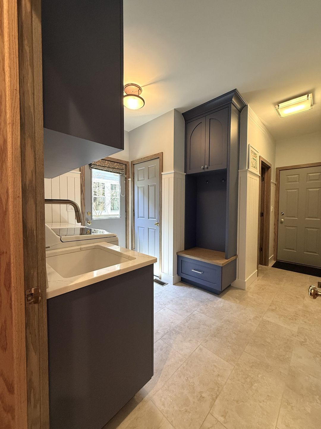 Mudroom room with navy blue built-in bench, upper locker cabinet, laundry sink, and dark cabinetry - Kelly Thayer Design