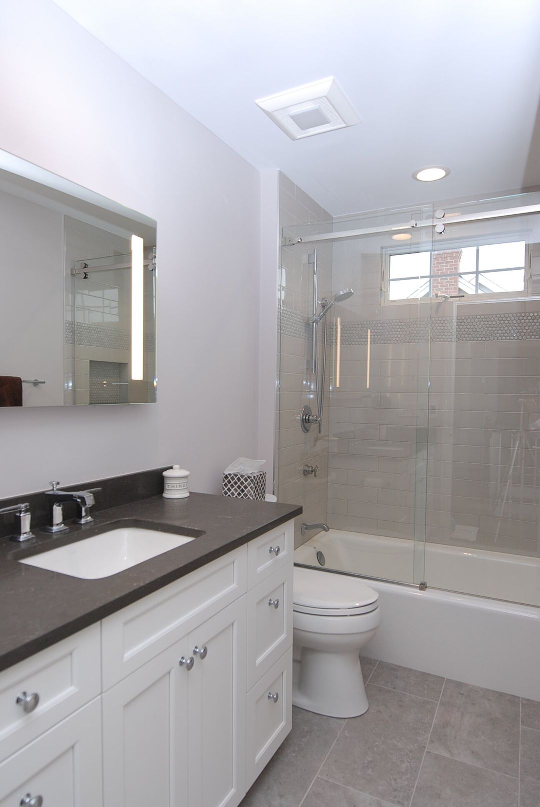 Hawthorn Woods hall bathroom with white shaker vanity, dark quartz countertop, and frameless glass tub surround - Kelly Thayer Design