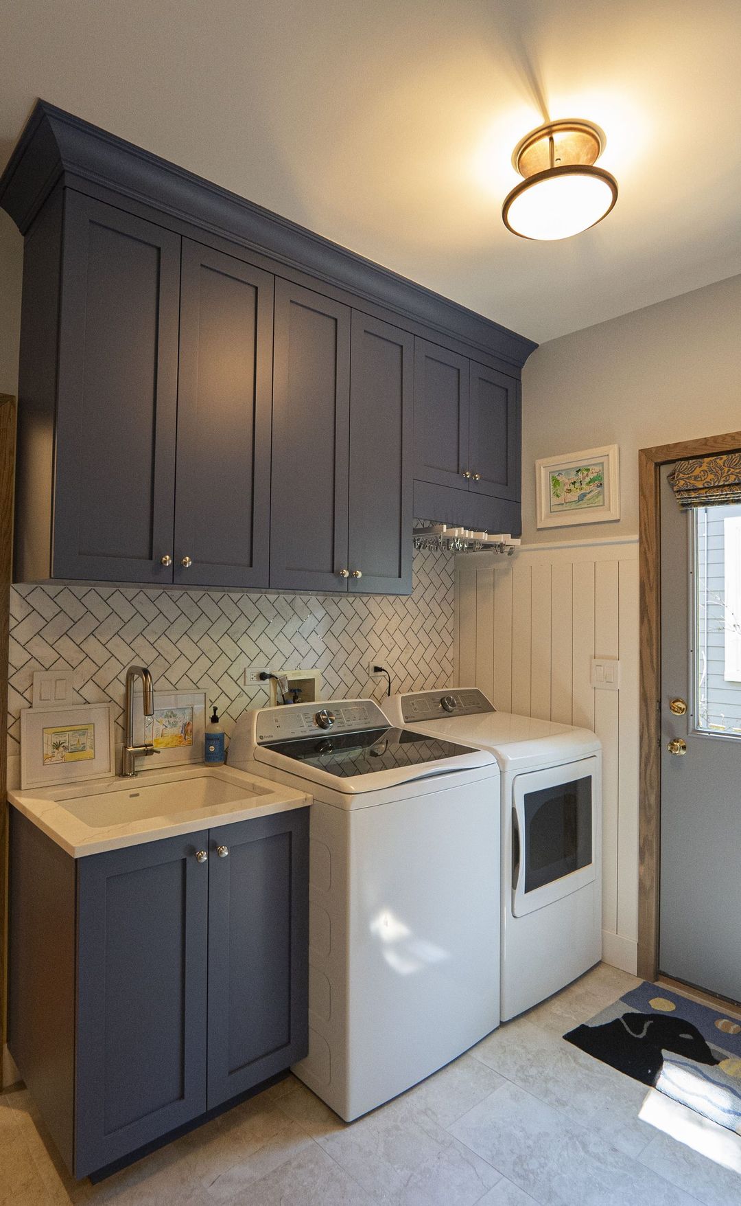 Laundry room with navy shaker cabinets, herringbone tile backsplash, utility sink, shiplap wainscoting, and top loader washer dryer - Kelly Thayer Design