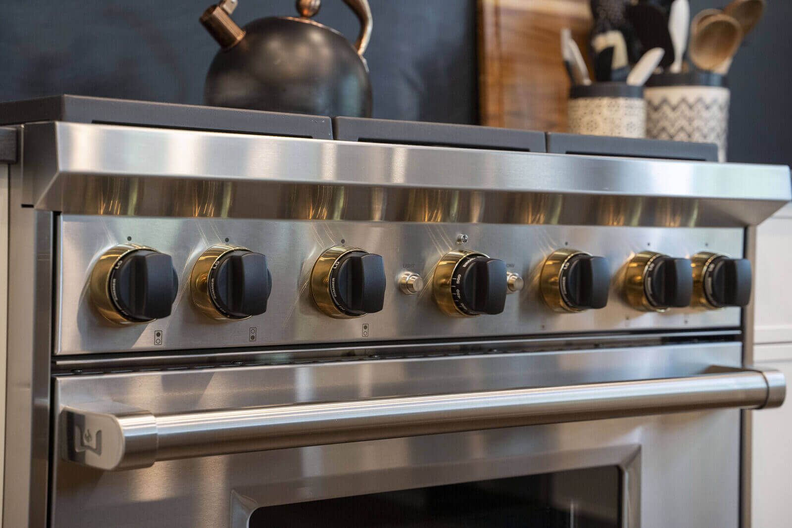 Northbrook Kitchen Remodel - Hidden Storage | Kelly Thayer Design Close-up of Wolf range brass knobs in black and white Kildeer kitchen remodel