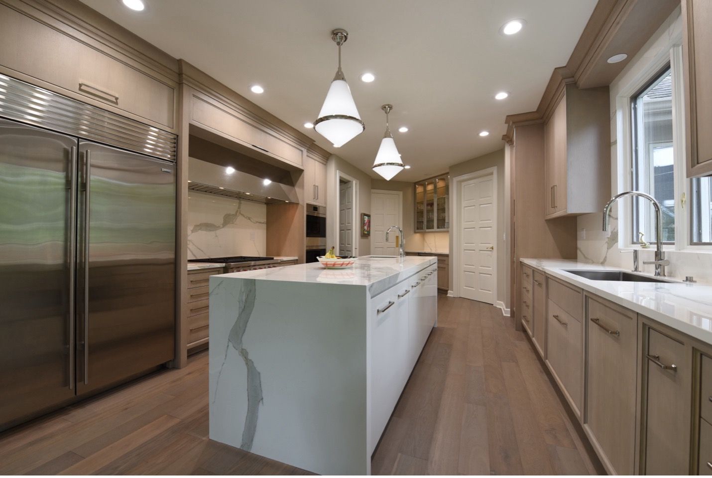 Northbrook kitchen with warm wood inset cabinetry, porcelain waterfall island and full-height backsplash, polished stainless steel custom hood, and Sub-Zero columns